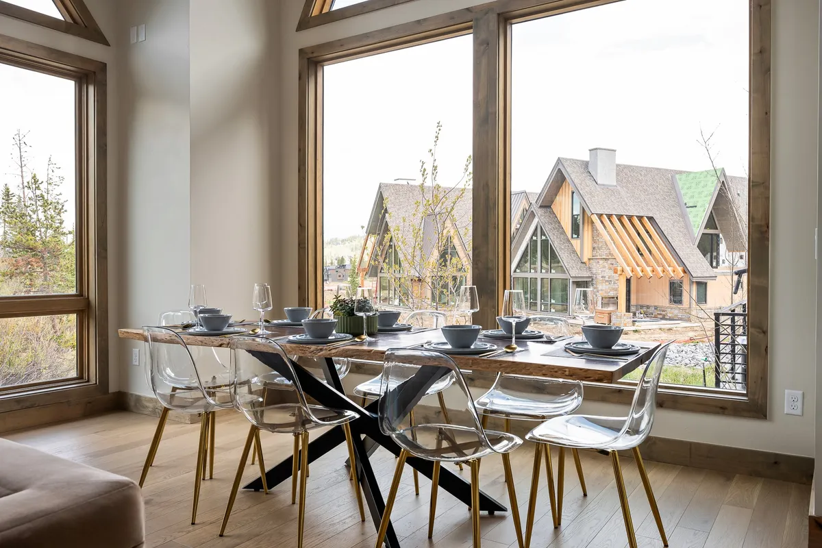 A large dining table with comfortable chairs sits in front of floor-to-ceiling windows, flooding the dining area with natural light and offering a scenic outdoor view. The setting suggests memorable family meals or entertaining guests with the beauty of the landscape as a backdrop.