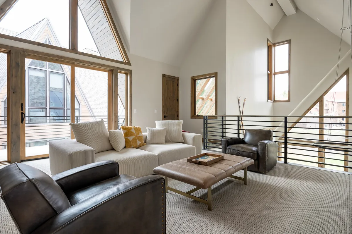 A welcoming seating area with large windows, comfortable armchairs, and a textured area rug, bathed in natural light. The setting encourages guests to unwind, socialize with friends, and take in the sunset or mountain scenery after a day outside.
