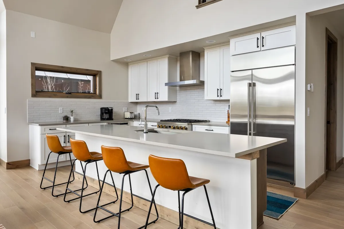 The kitchen is anchored by a spacious island with bar stools, stainless steel appliances, and a large window. The setup invites casual conversation and offers a view, making it ideal for both cooking and gathering with family or friends.