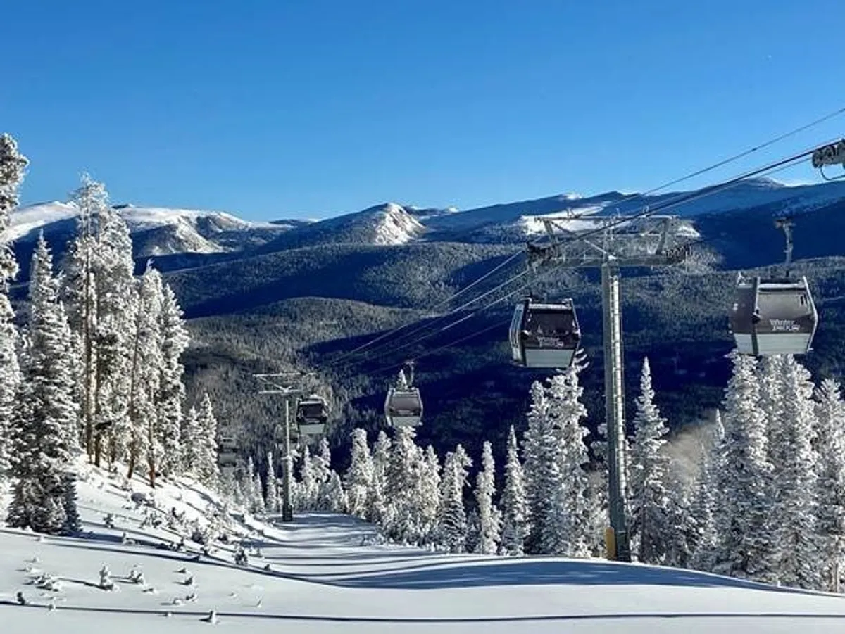 An inviting exterior scene of ski lift gondolas gliding above snow-covered mountains framed by pine trees. The image exudes possibilities for outdoor adventure and group exploration in a beautiful alpine setting, set just outside the chalet's doorstep.