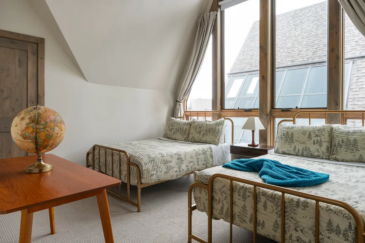 A restful bedroom with two beds dressed in patterned bedding, a wooden globe on a side table, and a table lamp providing a warm glow. The scene evokes comfort, togetherness, and a spirit of adventure—perfect for siblings or friends sharing a space.