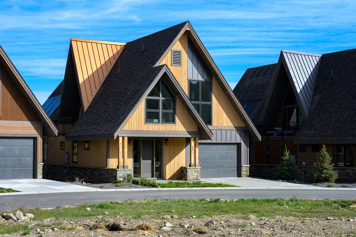 The image showcases a stunning A-frame chalet with rich wooden siding, large windows that invite natural light, and elegant stone accents. The spacious porch overlooks a scenic yard, perfect for unwinding as the sun sets over the Colorado mountains. The setting exudes warmth and comfort, hinting at memorable family gatherings and relaxing outdoor experiences.