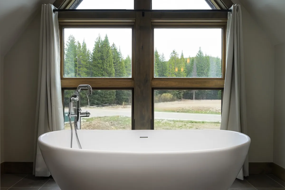 A freestanding bathtub is centered by expansive windows that overlook a forested landscape. The scene radiates tranquility, inviting guests to indulge in spa-like relaxation while soaking in the beauty of the outdoors. The abundant natural light enhances the sense of luxury and wellness.