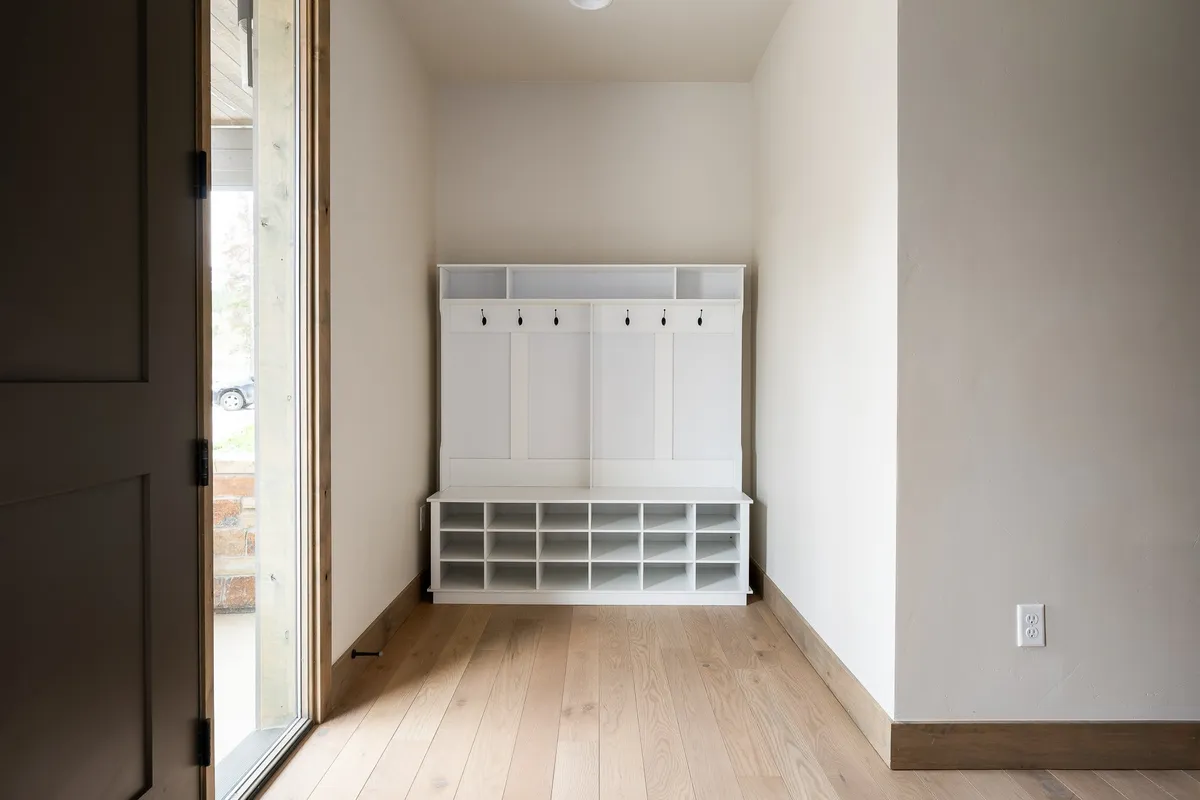 A functional mudroom or gear storage area with a bench, hooks for coats, and wooden flooring—designed for easy organization of outdoor gear upon returning from mountain adventures.